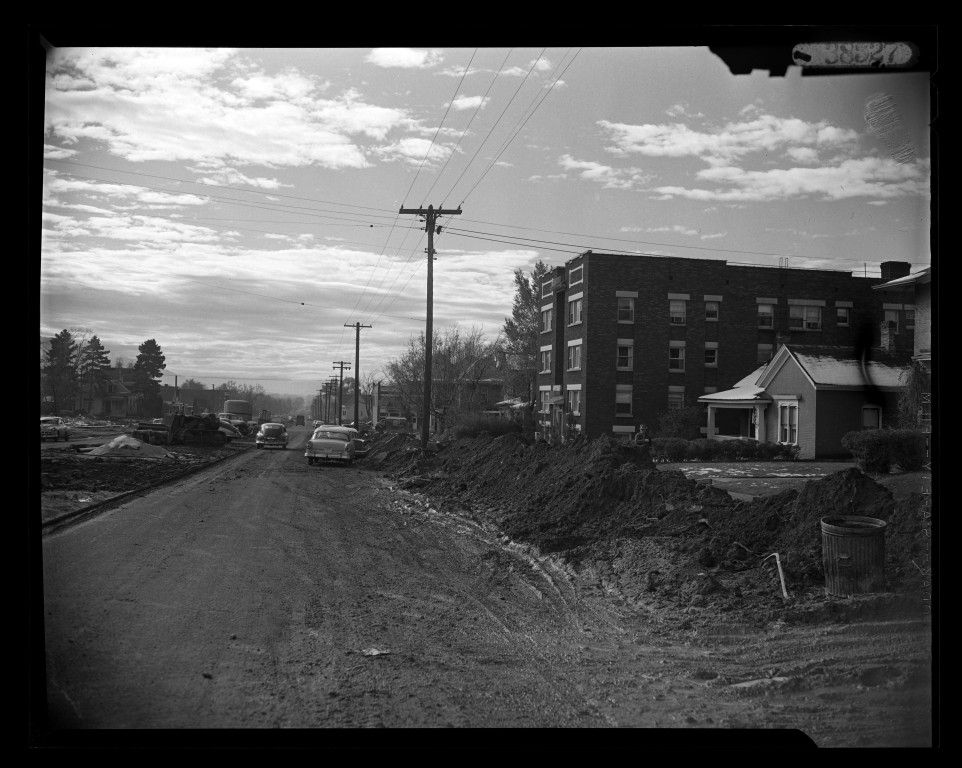 Road excavation beside homes and an apartment building along 700 East in 1956